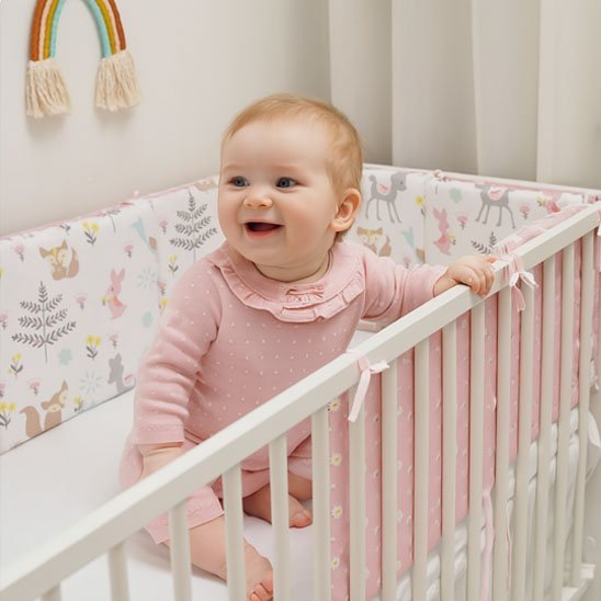 beau bébé assis au lit avec tour de lit bébé pastel