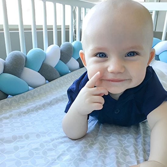 bebe sur son ventre sourit dans lit avec tresse de lit multicolore